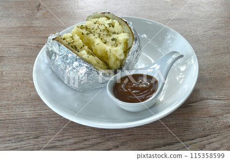 baking mashed potato with cheese in foil dressing salty gravy sauce on plate baking mashed potato with cheese in foil dressing salty gravy sauce on plate 115358599