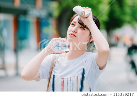 一名年輕女子忍受酷熱,用塑膠瓶冷卻頭部 一名年輕女子忍受酷熱,用塑膠瓶冷卻頭部 115359217