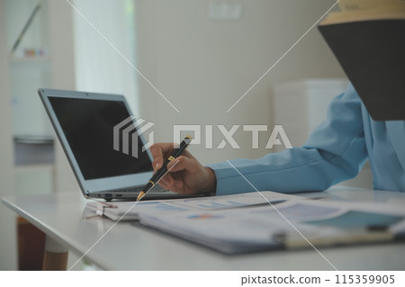 Charming Young asian businesswoman sitting on laptop computer in the office, making report calculating balance Internal Revenue Service checking document. 115359905