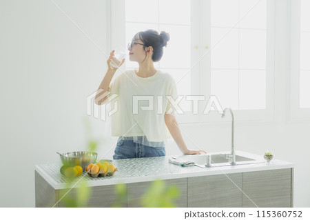 Woman drinking water in the kitchen 115360752