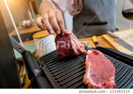 Chef at the kitchen preparing beef steaks on the home electric grill Chef at the kitchen preparing beef steaks on the home electric grill 115361515