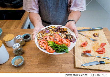 Chef at the kitchen preparing grilled eggplants with garlic 115361596