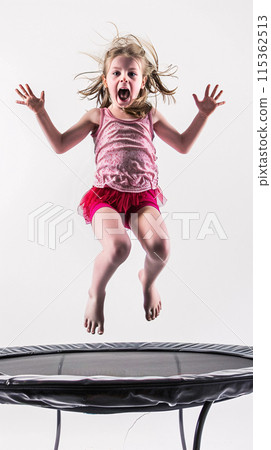 child jumping on a trampoline, their body suspended in mid-air against the white backdrop 115362513