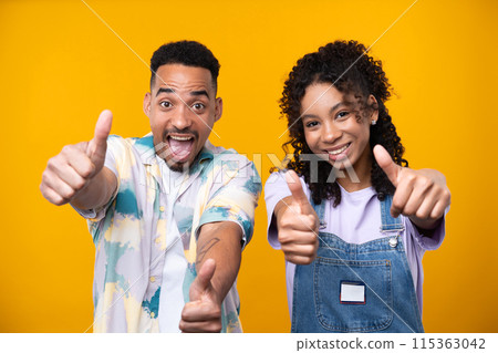 Two hipster friends smiling cheerfully while standing against a yellow background. High quality photo Two hipster friends smiling cheerfully while standing against a yellow background. High quality photo 115363042