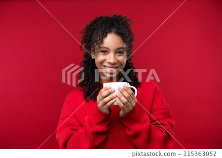 Portrait of a young girl smiling at the camera while standing against a red background. Happy black woman embracing her natural hair. 115363052