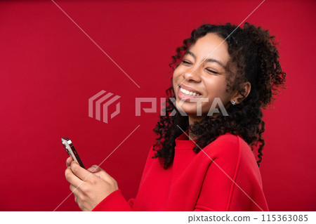 Portrait of a young girl smiling at the camera while standing against a red background. Happy black woman embracing her natural hair. Portrait of a young girl smiling at the camera while standing against a red background. Happy black woman embracing her natural hair. 115363085