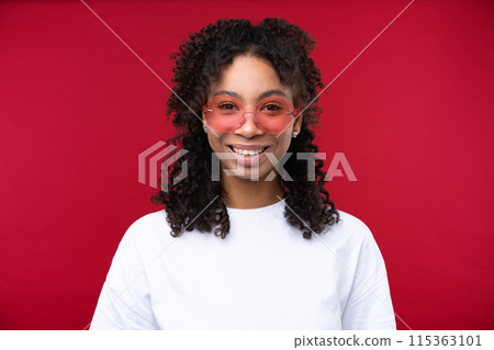 Portrait of a young girl smiling at the camera while standing against a red background. Happy black woman embracing her natural hair. Portrait of a young girl smiling at the camera while standing against a red background. Happy black woman embracing her natural hair. 115363101