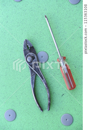 Pliers and a screwdriver on a green background. Tools. Pliers and a screwdriver on a green background. Tools. 115363108