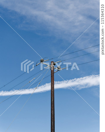 A rusted utility pole with insulators and wires stands against a cloudy sky, showcasing aged electrical infrastructure. 115364310
