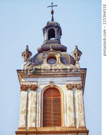 Church Dome and Cross. Dome and cross atop a baroque church, serene sky backdrop, indicating a place of worship. 115364318