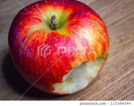 Half-Eaten Apple. A vibrant red apple, partially eaten, against a wooden backdrop, suitable for nutrition and diet content. Half-Eaten Apple. A vibrant red apple, partially eaten, against a wooden backdrop, suitable for nutrition and diet content. 115364344