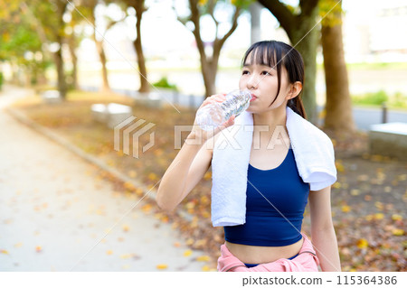 秋天沿著路邊樹散步的年輕女性、飲食、身體化妝、運動習慣、用塑膠瓶補水 115364386