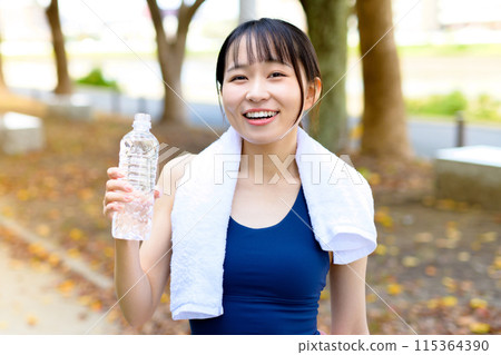 Young woman walking along a road lined with autumn trees, diet, body makeover, hydration with a plastic bottle, trimming Young woman walking along a road lined with autumn trees, diet, body makeover, hydration with a plastic bottle, trimming 115364390
