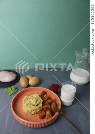 Serving lunch, potatoes with sausages, a glass of milk and ingredients for cooking, potatoes, chicken breast, milk on a gray background, space for copyspace text 115365398