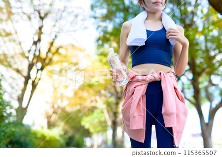 A young woman jogging along a road lined with trees in an autumn park; dieting, bodybuilding, towel in hand A young woman jogging along a road lined with trees in an autumn park; dieting, bodybuilding, towel in hand 115365507