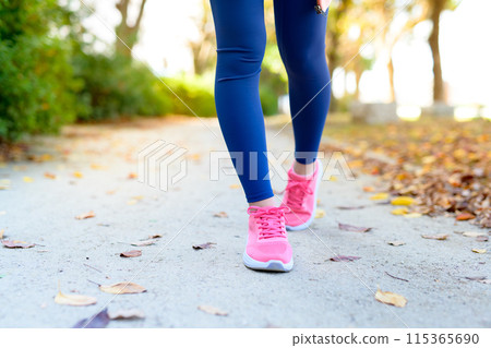 Feet of a young woman jogging along a roadside tree in an autumn park Diet Body makeup Front view 115365690