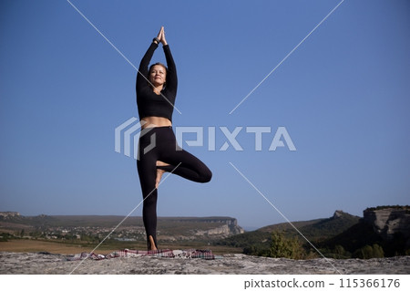A woman is doing yoga on a rock in a beautiful mountain setting A woman is doing yoga on a rock in a beautiful mountain setting 115366176