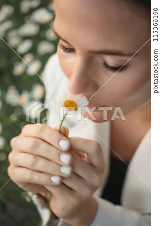 A woman is smelling a flower. The flower is yellow and white. 115366190