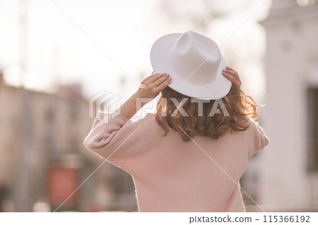A woman wearing a white hat and a pink sweater stands in front of a building 115366192