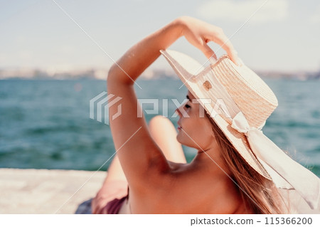 A woman in a swimsuit sits with her back holding a hat, looks at the ocean, sunny day, relaxes. A woman in a swimsuit sits with her back holding a hat, looks at the ocean, sunny day, relaxes. 115366200