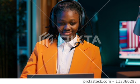 Student listening to music while she writes her essays at home, enjoying groovy tunes on headphones. Young woman creating a relaxing atmosphere to finish homework and tasks. Camera A. 115366285