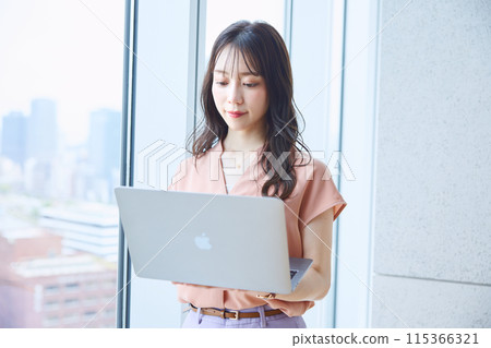 Woman looking at a computer by the window in an office 115366321