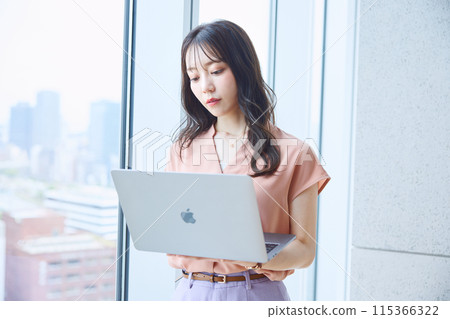 Woman looking at a computer by the window in an office 115366322