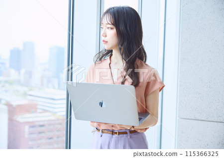 一位女士在辦公室窗邊看著電腦 115366325