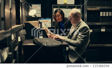 Team members cross reference data to track down potential suspect, using archived records and forensic evidence reports. Officers uncover crucial information to help solve legal case. Camera B. 115366356