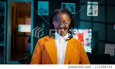 Portrait of african american student putting glasses on and working on english essays at home, reading academic databases for additional resources. Young woman studying at university. Camera B. 115366359
