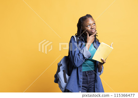 Portrait of BIPOC woman daydreaming while holding book, thinking of characters. Person with novel in arms caught in imagination while enjoying leisure time, isolated over studio background Portrait of BIPOC woman daydreaming while holding book, thinking of characters. Person with novel in arms caught in imagination while enjoying leisure time, isolated over studio background 115366477
