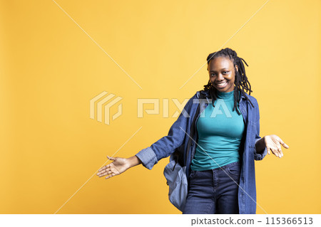 Happy young woman doing shrugging shoulders gesture, showing relaxed mood. Serene BIPOC girl doing nonchalant carefree hand gesturing, isolated over yellow studio background Happy young woman doing shrugging shoulders gesture, showing relaxed mood. Serene BIPOC girl doing nonchalant carefree hand gesturing, isolated over yellow studio background 115366513