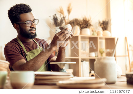 Dark-skinned man at the table with piece of clay in hands 115367077