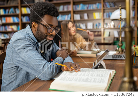 Curly-haired bearded african american man in the library looking thoughtful Curly-haired bearded african american man in the library looking thoughtful 115367242