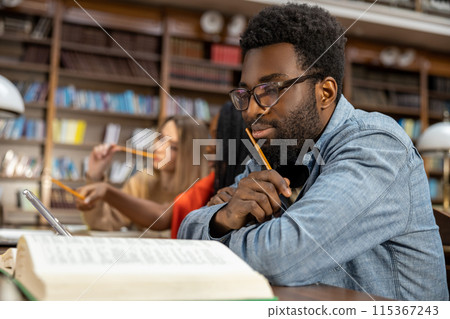 Curly-haired bearded african american man in the library looking thoughtful 115367243