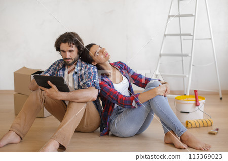 Focused Couple with Tablet Relaxing on Floor for DIY Home Makeover 115369023
