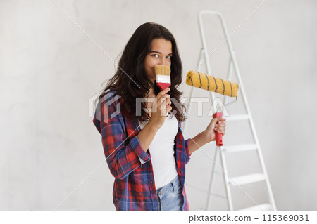 Playful Young Woman Holding Paint Supplies for DIY Home Renovation 115369031