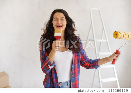 Joyful Young Woman Singing with Paint Supplies During Home Renovation 115369119