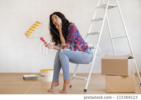 Thoughtful Woman Holding Paint Roller Sitting on Ladder for Home Renovation 115369123