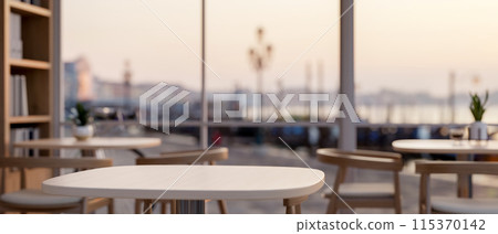 A table in a minimalist coffee shop or restaurant seating area by a window with a city view. 115370142