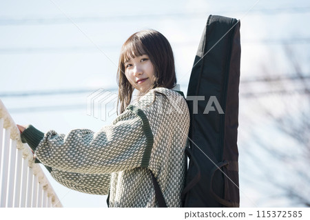 Young woman carrying a guitar case outdoors 115372585