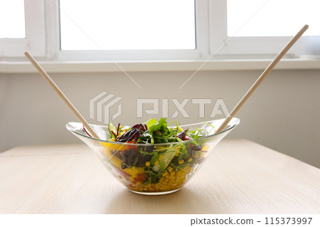 wooden spoons stir salad in a glass plate corn tomatoes cucumbers bulgarian yellow peppers arugula leaves vegetarian food lunch slimming diet close-up female hands 115373997
