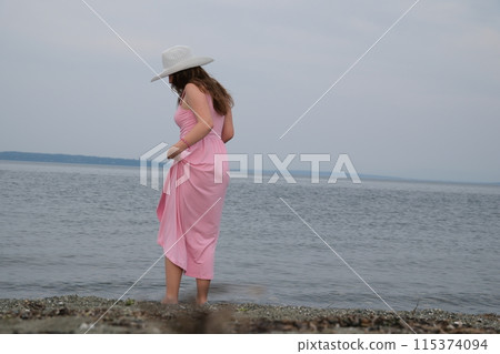 White hat Girl in a pink dress on the ocean A wide shot of a teen strolling barefoot at the beach White hat Girl in a pink dress on the ocean A wide shot of a teen strolling barefoot at the beach 115374094