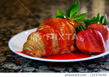 Pouring strawberry syrup on sweet croissants on white plate. Delicious croissants for breakfast or snack  115374240