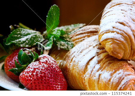 Croissant on the white plate, with fresh strawberry and whipped cream. Croissants and fresh raspberries on dessert plate on gray wooden table. 115374241