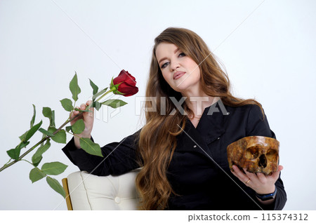 insidious cruel woman vamp strong serious woman in her hands with a rose and a human skull sits on a white background in black clothes medicine power love Lost opportunities Life and death 115374312