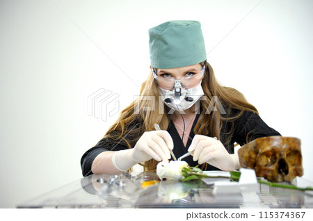 Illuminator with safety glasses and binoculars woman doing surgery showing demonstrating on a flower with scalpel next to skull blank text surgical latex gloves black clothes doctor's green cap Illuminator with safety glasses and binoculars woman doing surgery showing demonstrating on a flower with scalpel next to skull blank text surgical latex gloves black clothes doctor's green cap 115374367