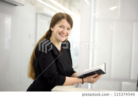Image of young woman, company worker smiling and holding notepad standing against Image of young woman, company worker smiling and holding notepad standing against white background 115374549