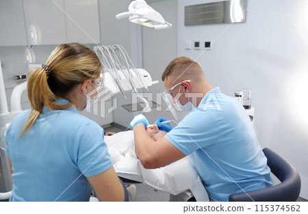 getting teeth cleaning and polishing at clinic Dentist working on patient in chair. doctor in blue gloves applies ointment to patient's teeth that shows where there is plaque that needs to be cleaned. 115374562