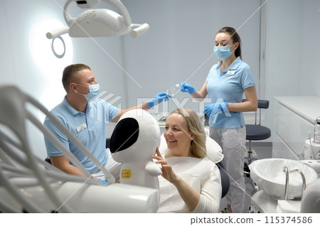 dental clinic middle aged woman sitting in chair with astronaut soft toy smiling pretty showing child that it's safe to sit fear of dentistry children nurse handing goggles to doctor dental clinic middle aged woman sitting in chair with astronaut soft toy smiling pretty showing child that it's safe to sit fear of dentistry children nurse handing goggles to doctor 115374586
